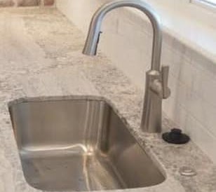 Undermount stainless steel sink and curved faucet fitted into a light patterned countertop